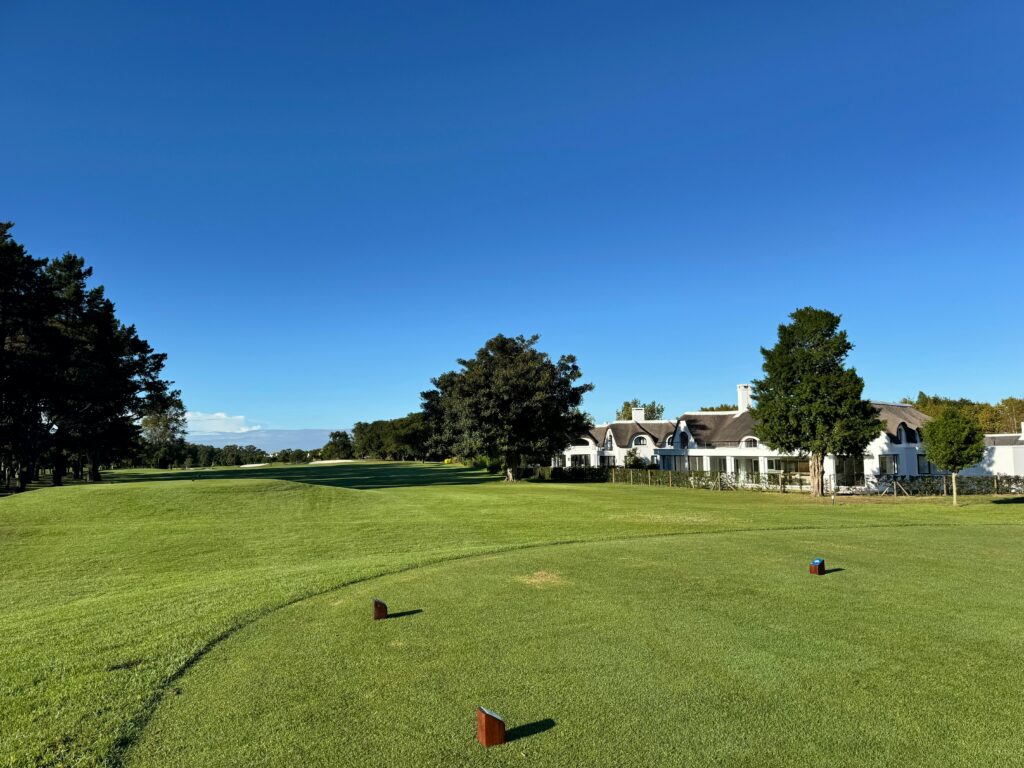 A picturesque view of a golf course fairway with a clubhouse and lush greenery under a clear blue sky.